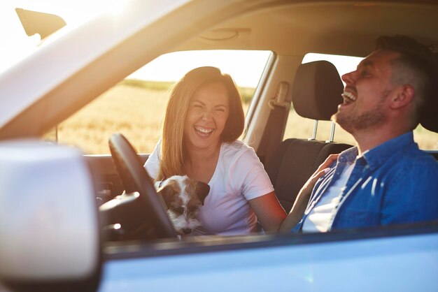 Foto um casal sorridente com um cão sentado no carro