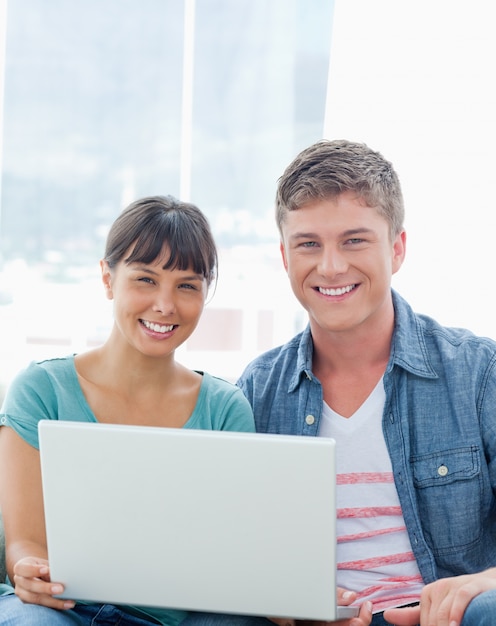 Um casal sorridente com um laptop enquanto olham para a câmera