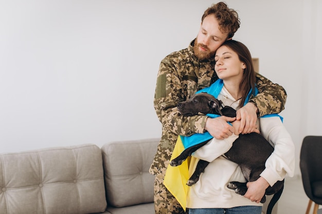 Um casal ucraniano, um soldado em uniforme militar e uma garota embrulhada em uma bandeira ucraniana seguram um cachorro nos braços felizes juntos