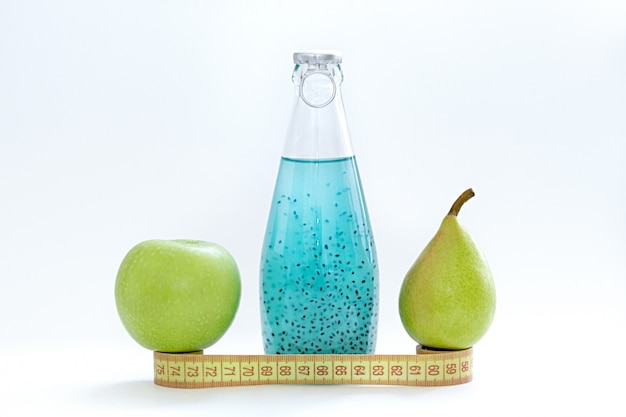 Um centímetro, uma maçã, uma pêra e garrafas de vidro com semente de manjericão azul ficar em um fundo branco