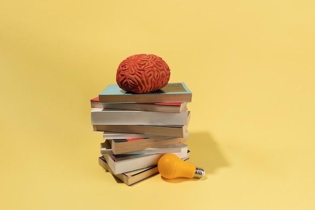 Um cérebro, uma lâmpada e livros sobre ideias de conceito criativo de fundo amarelo