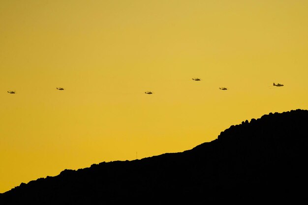 Um céu amarelo com uma silhueta de helicópteros voando ao longe.