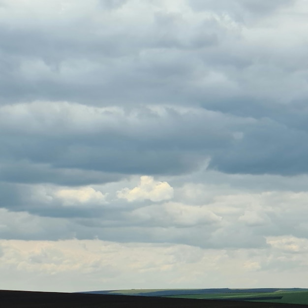 Um céu nublado está sobre um campo e um campo com uma vaca e um homem a cavalo.