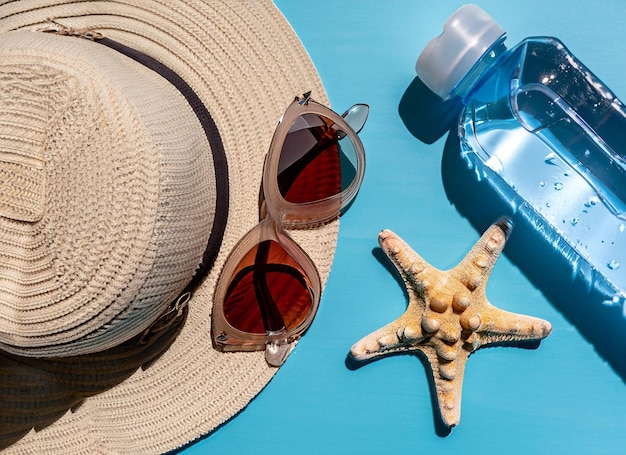 Um chapéu, óculos de sol e uma garrafa de água estão sobre uma mesa azul.