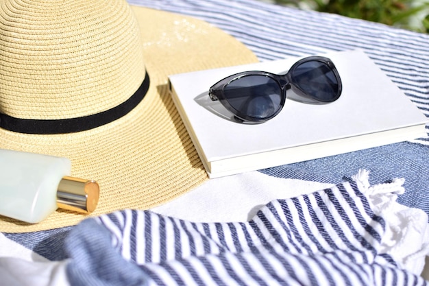 Um chapéu, óculos escuros e um livro estão sobre uma toalha de praia.