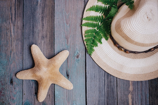 Um chapéu, uma folha de samambaia, uma estrela do mar, conchas do mar no fundo de madeira