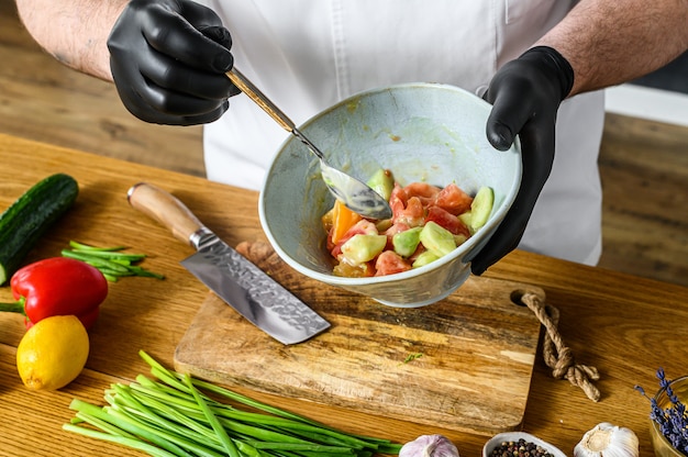 Um chef em luvas pretas prepara uma salada de vegetais vegetariana.