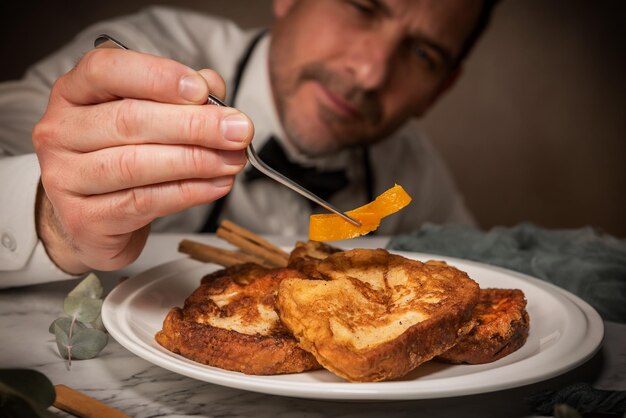 Um chef garçom coloca raspas de laranja em um conjunto de torrijas gourmet com pinças Um doce típico espanhol