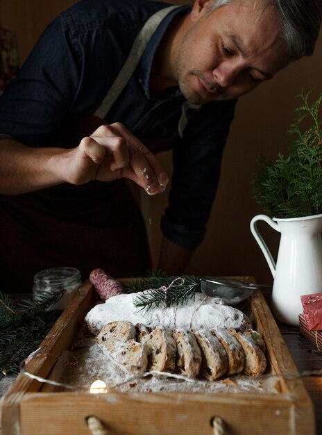 Um chef masculino prepara um stollen para um bolo de stollen de natal em estilo rústico de açúcar em pó