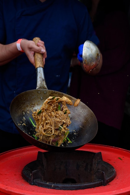Um chef prepara comida chinesa em um festival de comida de rua Fotografado enquanto a comida voa sobre uma frigideira cheia de fogo e fumaça
