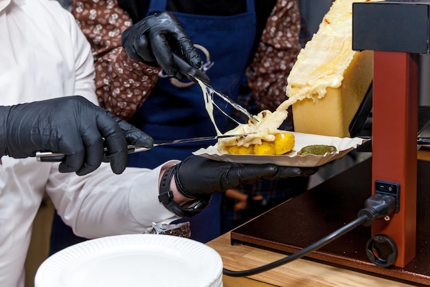 Um chef prepara um prato com raclette usando um instrumento especial para derreter queijo.