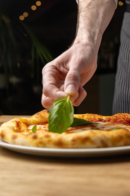 Um chef prepara uma pizza com folhas de manjericão em um prato.