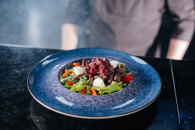 Um chef profissional serve uma salada fresca de tomate e vitela com molho em close-up de um restaurante gourmet.