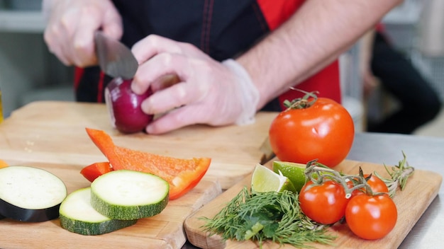 Um chef trabalhando na cozinha cortando a cebola vegetais diferentes em primeiro plano