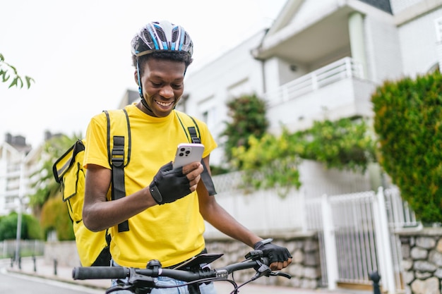 Um ciclista africano sorridente verificando seu telefone durante um turno de entrega de comida