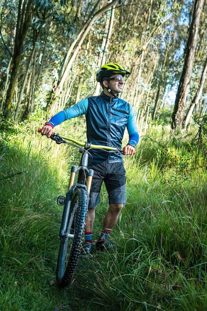 Um ciclista de montanha fica na floresta com sua bicicleta ao fundo