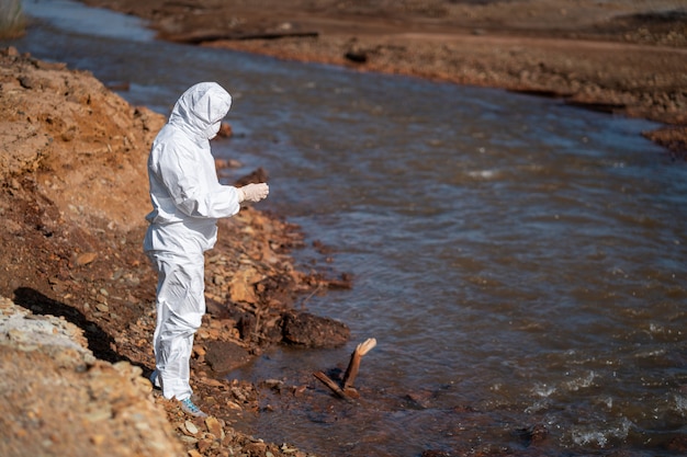 Um cientista em um traje de proteção branco coleta amostras de água de um rio poluído.