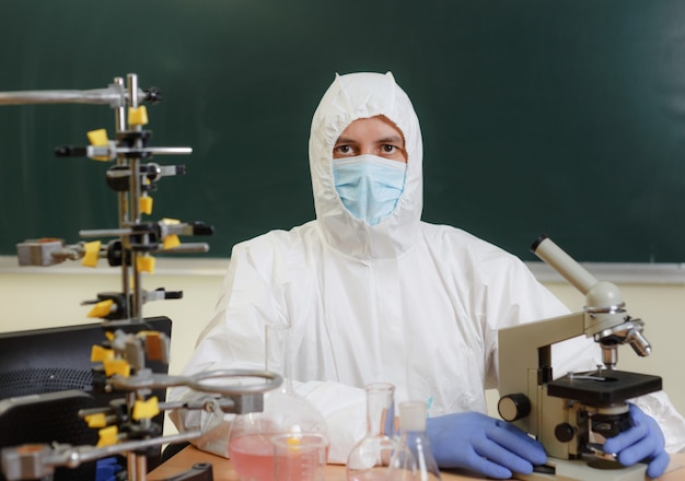 Um cientista químico em um traje de proteção está sentado em seu laboratório, há muitos equipamentos químicos ao redor.