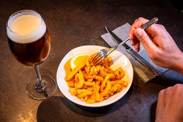 Um cliente comendo lula à milanesa com limão acompanhada de uma cerveja em um fundo preto em um pedacinho