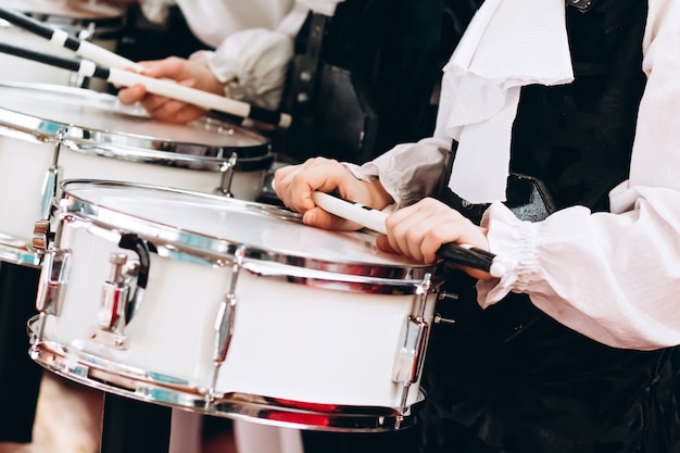 Um close das mãos de um baterista em um desfile. conjunto infantil em camisas brancas. tarola nova branca, paus brancos. o conceito de uma parada militar e de março.