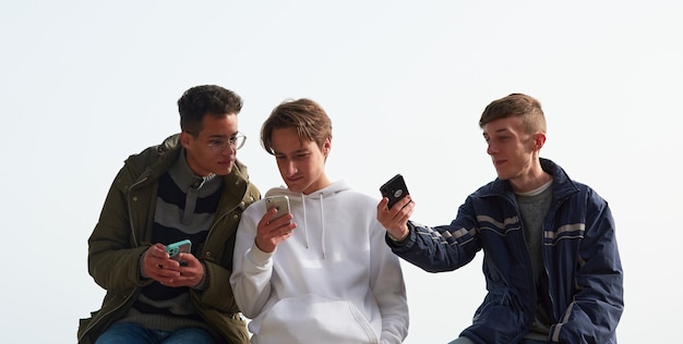 Um close de três jovens caucasianos e hispânicos se socializando e usando seus smartphones