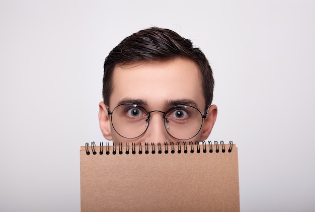 Um close de um jovem de óculos espreitando por trás de um notebook.