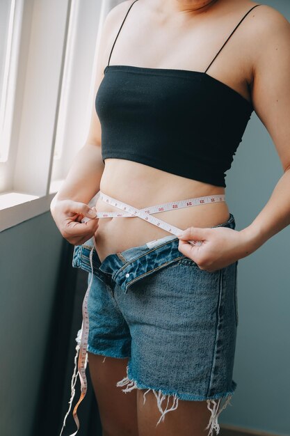 Foto um close de uma barriga com cicatriz de secção e gordura abdominal saúde das mulheres uma mulher vestida com roupas esportivas demonstrando seu corpo imperfeito após o parto com o berçário ao fundo