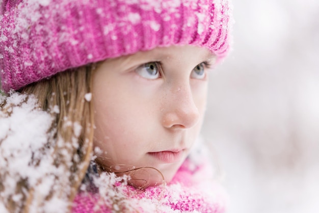 Um close de uma criança de olhos azuis com neve no cabelo está olhando para cima