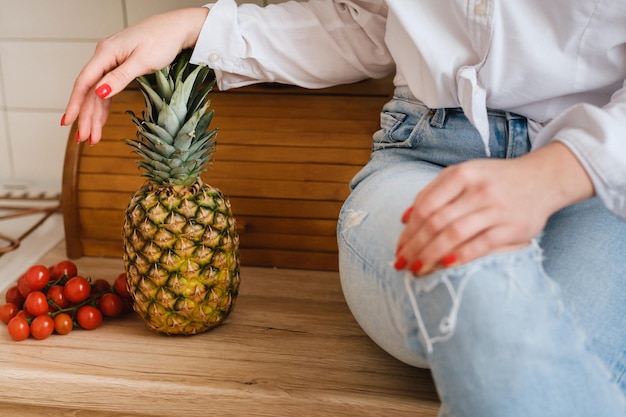 Um close de uma dona de casa em uma camisa branca e jeans está sentado em uma mesa e frutas e legumes estão por perto O conceito de alimentação saudável