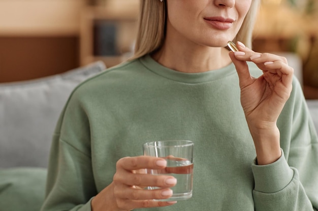 Foto um close de uma mulher a tomar uma pílula de vitaminas