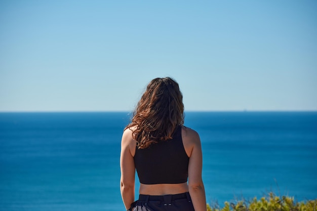 Um close de uma mulher por trás olhando para o mar