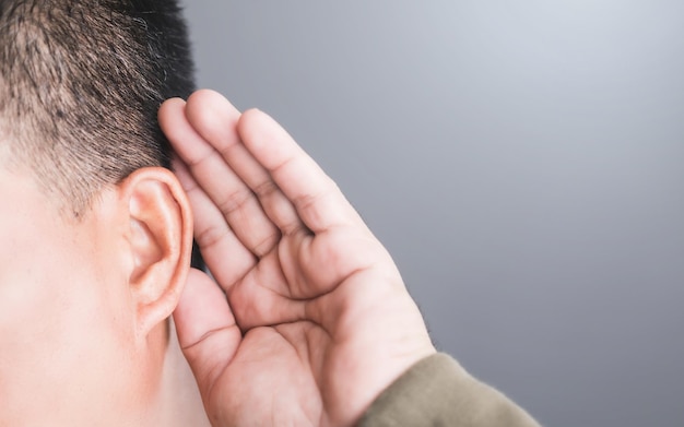 Um close de uma pessoa colocando a mão atrás da orelha, indicando dificuldades auditivas Esta imagem destaca os desafios da perda auditiva e a importância da conscientização sobre a saúde da orelha