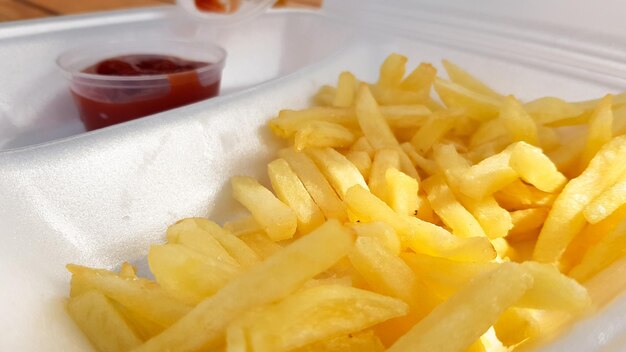 Um close-up de batatas fritas de amarelo alaranjado dourado com ketchup servido em um recipiente de espuma. Fast food para viagem. Alimentos frescos indesejados.