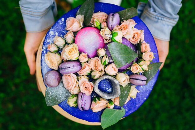 Um close-up de um bolo decorado com rosas vivas com folhagem verde e macaroons