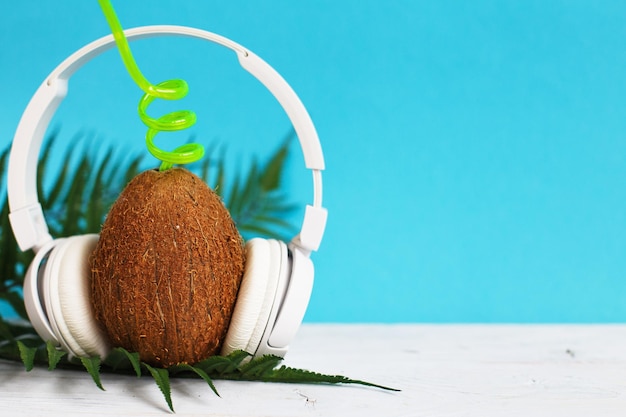 Um coco com palha e fones de ouvido em um fundo azul Espaço de cópia do conceito de verão e viagem