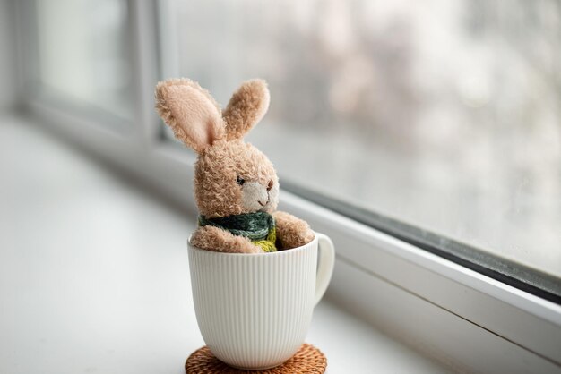 Foto um coelho em um cachecol, sentado e olhando pela janela, um coelho de pelúcia, o conceito de solidão