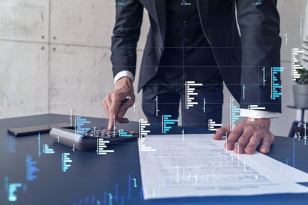 Um comerciante computando dados históricos para prever o comportamento do mercado de ações Conceito de negociação na Internet Forex e gráfico de holograma financeiro sobre a mesa e a calculadora