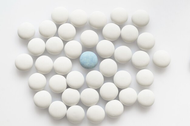 Um comprimido azul e muitos brancos sobre uma superfície clara