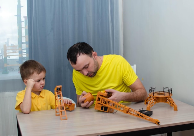 Um conceito de gente - um pai feliz e um filho pequeno brincam. Filho de família feliz e jovem pai amoroso passam tempo de lazer juntos, brincam, constroem guindaste de brinquedo.