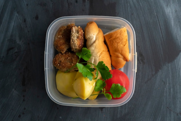 Um conceito de hora de almoço, comendo do recipiente de plástico com carne e batatas nas mesas