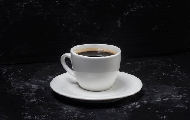 Foto um conceito minimalista de uma xícara de café e que fica sobre um fundo preto abstrato.