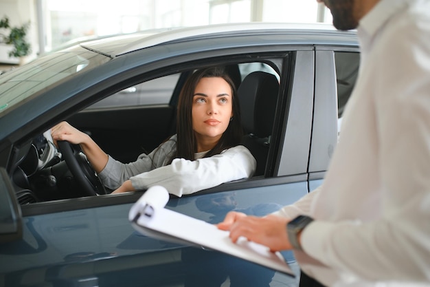 Um concessionário de veículos amigável mostrando um carro novo a uma jovem.