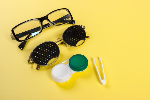 Um conjunto de acessórios para visão. Óculos pinhole, lentes com recipiente e óculos para visão. Par de médicos pinhole óculos com reflexões.