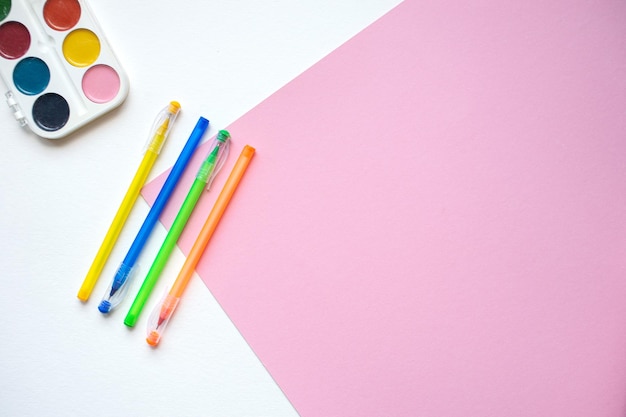 Um conjunto de artigos de papelaria em canetas de fundo branco e rosa de diferentes cores e aquarela