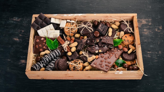 Um conjunto de chocolate ao leite e chocolate preto em uma caixa de madeira com nozes e biscoitos em um fundo preto de madeira copie o espaço para texto