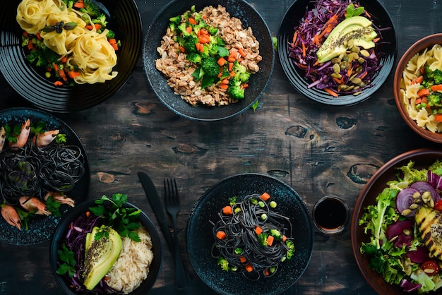 Um conjunto de comida e pratos Salada de risoto de arroz de macarrão Em um fundo preto Espaço para texto grátis