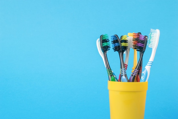 Um conjunto de escovas de dentes em um copo de plástico amarelo sobre fundo azul