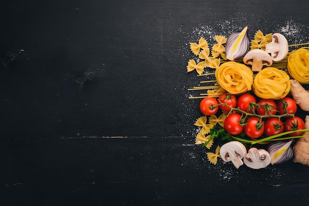 Foto um conjunto de macarrão macarrão espaguete tagliatelle fettuccine farfalle italiano cozinhando legumes frescos e especiarias em um fundo de madeira preto vista superior copiar espaço