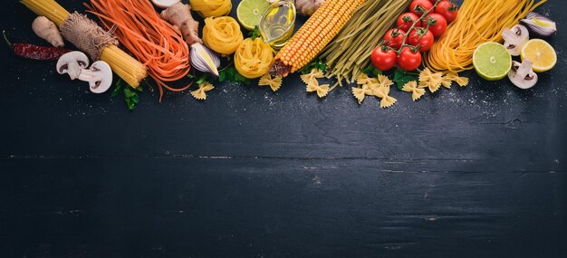 Um conjunto de macarrão macarrão espaguete tagliatelle fettuccine Farfalle italiano cozinhando legumes frescos e especiarias Em um fundo de madeira preto Vista superior Copiar espaço