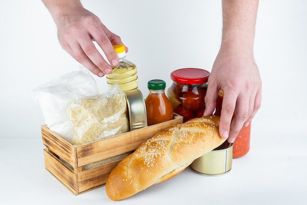 Um conjunto de produtos de armazenamento a longo prazo e as mãos dos homens em uma parede branca. Doações de alimentos ou conceito de entrega de alimentos